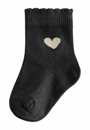 Black knit sock with a scalloped top edge and a small beige heart design. Made from a stretchy material, featuring a closed toe.