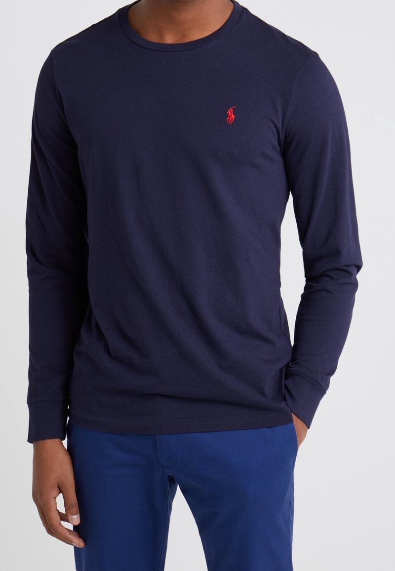 T-shirt a maniche lunghe blu navy in tessuto di cotone, con collo rotondo e un piccolo logo rosso sul lato sinistro del petto. Design semplice con una silhouette aderente.