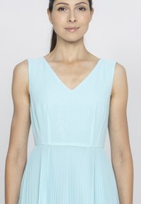 Jasnoniebieska sukienka bez rękawów z dekoltem w kształcie litery V, z plisowaną spódnicą i gładkim korpusem. Wykonana z miękkiego materiału o subtelnej fakturze.