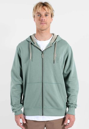 Sweat à capuche zippé en tissu vert doux. Comprend des poches avant, une capuche avec cordon de serrage et une doublure intérieure beige contrastante. Design simple, coupe décontractée.