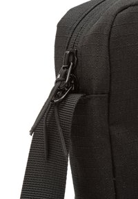 Nahaufnahme einer schwarzen Stofftasche, die einen Reißverschluss und einen Riemen zeigt, wobei die strukturierte Oberfläche und das stilvolle Design hervorgehoben werden.