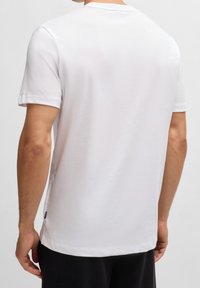 Biała koszulka z bawełny z krótkim rękawem, okrągłym dekoltem i prostym wykończeniem. Minimalistyczny design bez widocznych wzorów czy akcentów.