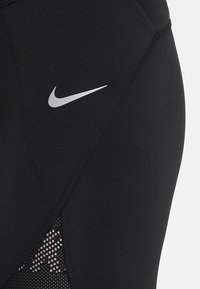 Czarne legginsy sportowe wykonane z elastycznego materiału. Charakteryzują się srebrnym logo Nike oraz siateczkowymi wstawkami w kropeczki.