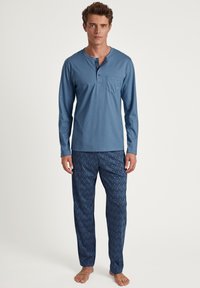 Chemise bleu clair à manches longues avec une poche et un col à boutons, associée à un pantalon de pyjama bleu foncé à motifs avec un design géométrique.