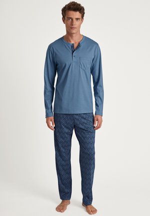 Chemise bleu clair à manches longues avec une poche et un col à boutons, associée à un pantalon de pyjama bleu foncé à motifs avec un design géométrique.