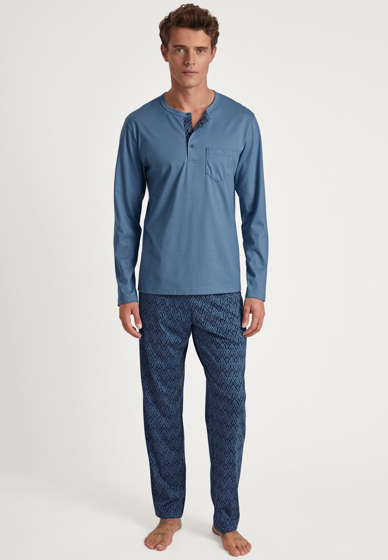Chemise bleu clair à manches longues avec une poche et un col à boutons, associée à un pantalon de pyjama bleu foncé à motifs avec un design géométrique.