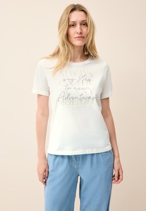 Witte katoenen t-shirt met korte mouwen, voorzien van gedrukte tekst in metallic en zwart, gecombineerd met lichtblauwe, loszittende spijkerbroek.
