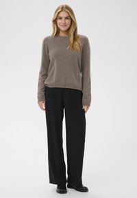 Pull tricoté marron clair à manches longues, col rond, associé à un pantalon large noir et des bottines noires. Design simple.