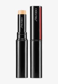 Palo de maquillaje negro con un núcleo beige claro, forma cilíndrica, acabado brillante, que presenta el logo de Shiseido y una línea de acento roja en uno de los lados.