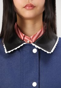 Denim jacket with a dark blue fabric, black leather collar with scalloped white trim, and a pink striped shirt underneath featuring a pearl button.