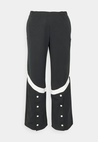 Svart vida byxor med vita diagonala ränder och tryckknappar som löper vertikalt nära fållarna på båda benen.