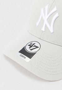 Jasnoszara czapka z daszkiem z białym wyhaftowanym logo i naklejką marki '47' na daszku.