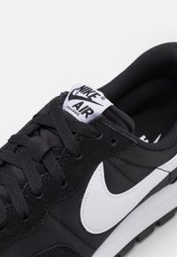 Musta Nike Air Pegasus -lenkkari, jossa on tekstuurinen musta päällinen, valkoinen nahkainen swoosh ja mustat nauhat. Pehmeä, vaahtomaisesti vuorattu sisus.