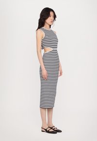 Stripet midikjole i svart og hvitt, med en tettsittende design og utskårne sider. Brukt med svarte slingback-sko. Glatt tekstur.