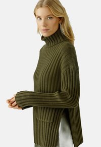 Olivgrüner gerippter Rollkragenpullover mit seitlichen Schlitzen, langen Ärmeln und lockerer Passform; verfügt über ein strukturiertes Strickmuster und funktionale Taschen.
