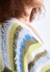 Multicolored knitted cardigan featuring stripes in green, blue, and white, with a fuzzy texture and open weave design.