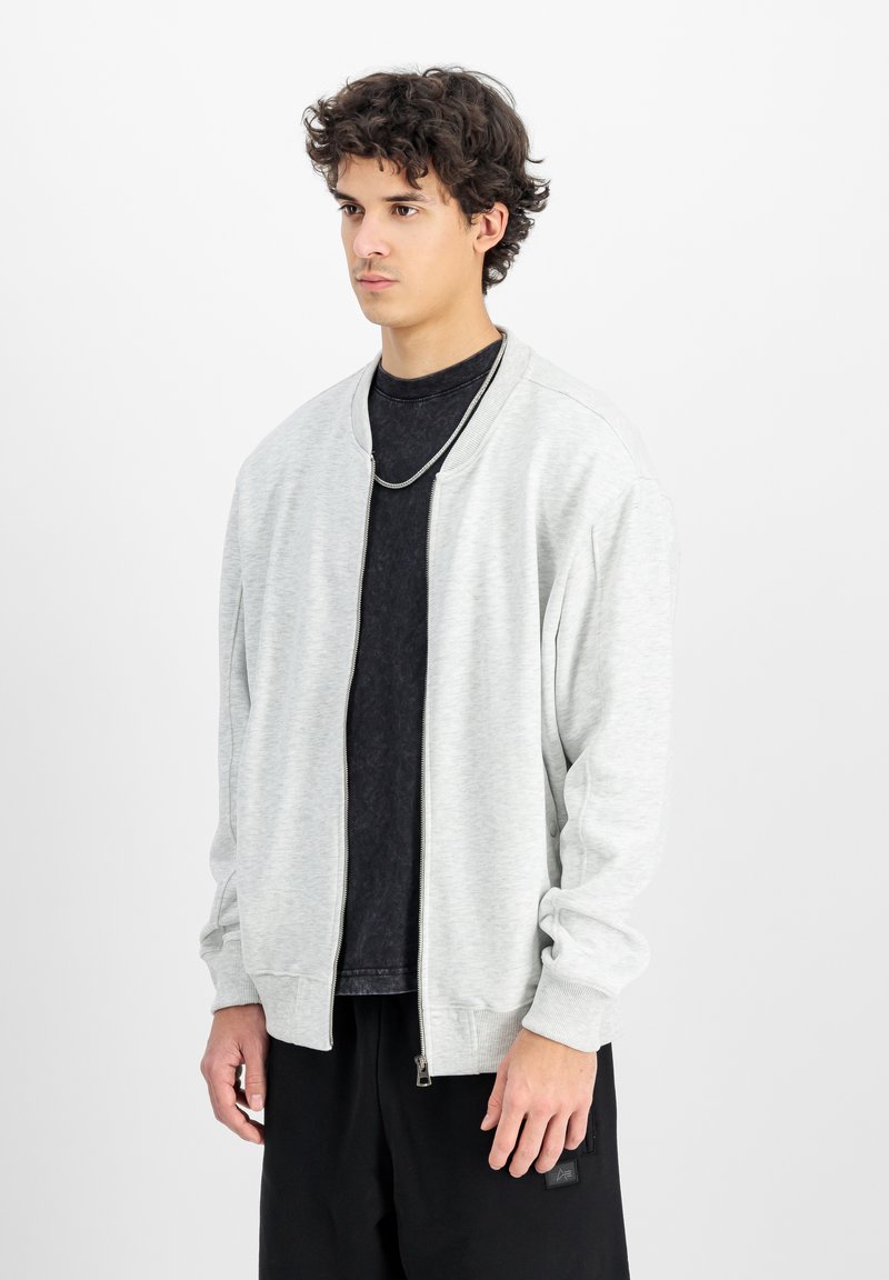 Svetločasna bomber jakna z zadrgo, izdelana iz mehkega materiala, z rebrastimi manšetami in robom, nosi se preko črne majice. Enostaven dizajn, brez vzorcev.