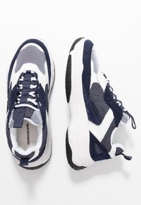 Marinblå och vita träningsskor med mesh, suède-accenter och en kraftig sula. Gummisula med texturerat grepp för bra fäste.