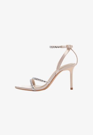 Nude high-heeled sandal with a glossy finish, multiple crossed straps, and a rhinestone-embellished ankle strap. Pointed toe design.