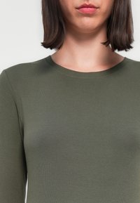 Haut à manches longues vert olive. Fabriqué en tissu côtelé avec un col rond. Texture lisse, silhouette ajustée et minimalisme dans les détails.