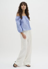 Lichtblauw off-shoulder top met pofmouwen, gecombineerd met losse witte broek. Zwarte flip-flops maken de outfit compleet.