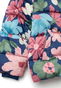 Chaqueta acolchada con un patrón floral en rosa, azul y verde sobre un fondo azul marino; presenta secciones acolchadas y puños acanalados.