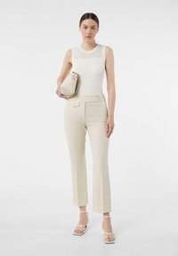 Hellbeige, gerippter, ärmelloser Top kombiniert mit cremefarbenen, taillierten Hosen mit zwei Fronttaschen und Knopfdetails sowie weißen, geschnürten Sandalen.