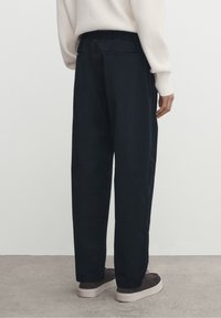 Svarta, löst sittande byxor med dragsko i midjan, sidofickor och en slät textur, bärs med grå sneakers.