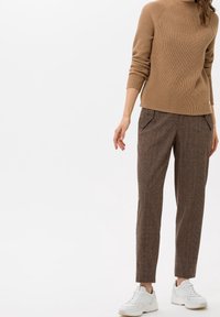 Pull en maille côtelée marron à manches longues associé à un pantalon marron à carreaux, fuselé, et des baskets blanches. Le pantalon comporte des poches avant.