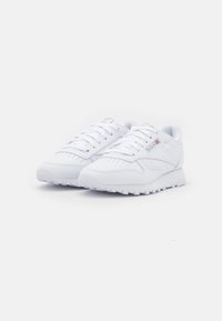 Weiße Sportschuhe mit einem glatten Lederobermaterial, runder Zehenpartie und flacher Gummisohle. Mit durchbrochenen Details und sechs Schnürlöchern.