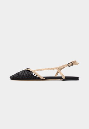 Flad sandal med spids tå, sort vævet front og beige flettede remme med ankel spænde på hvid baggrund.