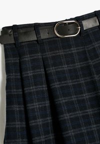 Plissé rok in donkerblauw van structuurstof met een ruitpatroon. Voorzien van een zwarte leren riem met een zilveren ovale gesp.