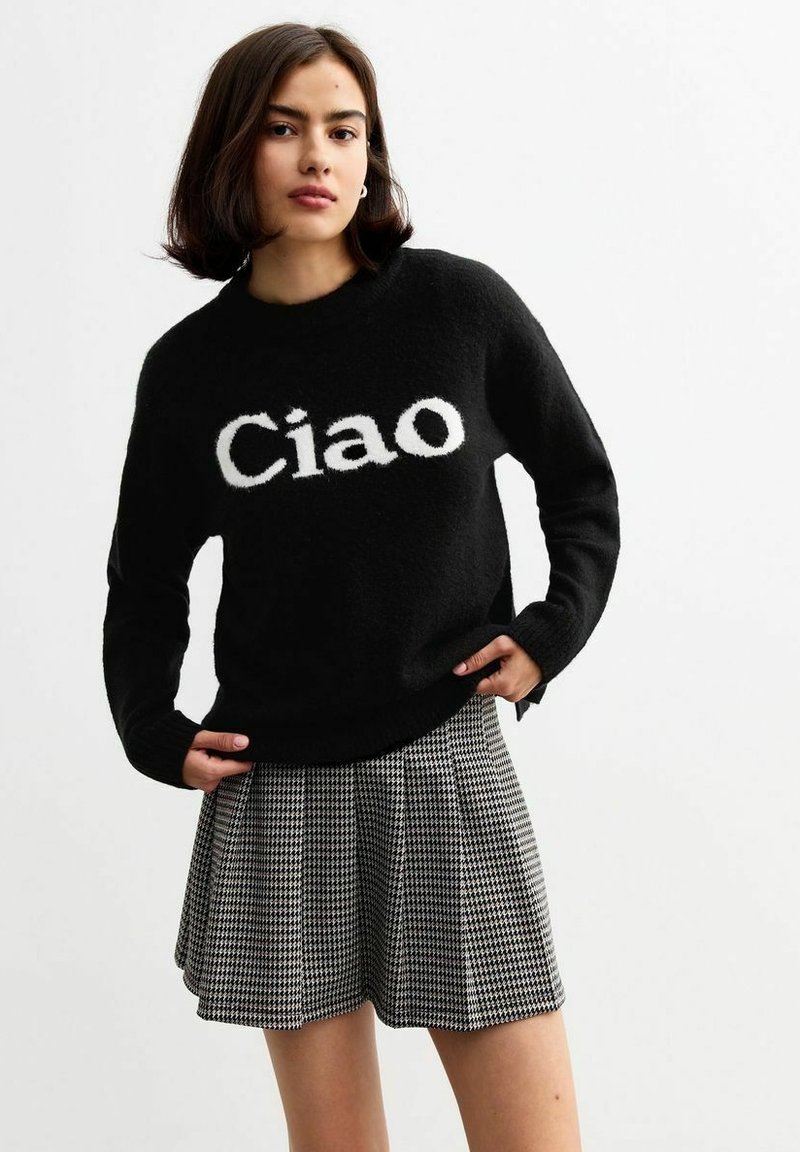 Suéter negro de punto con el texto blanco "Ciao", con mangas largas y cuello redondo, combinado con una falda plisada en blanco y negro de pata de gallo.