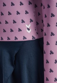 Zbliżenie na fioletową tkaninę z małymi, ciemnymi kwiatowymi wzorami oraz dwoma białymi ukośnikami skierowanymi w dół nad ciemnoniebieską, marszczoną tkaniną.