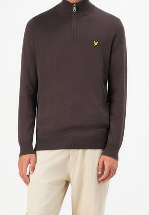Mand iført en mørkebrun quarter-zip sweater med en lille gul fuglelogo på brystet og beige bukser, vist fra nakke til hofter.