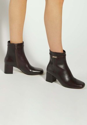 Brown leather ankle boots with a square toe, side zipper, and a block heel. Features a gold accent around the ankle area.