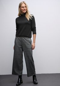 Zwarte coltrui, gecombineerd met grijze gestructureerde wijde broek en zwarte enkellaarsjes, heeft een ontspannen silhouet en lange mouwen.