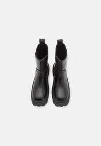 Botas de tobillo de cuero negro con acabado suave, paneles laterales elásticos y tiradores. Suelas de goma resistentes para tracción, diseño minimalista.