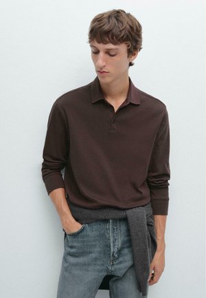 Brown long-sleeve polo shirt with three-button placket, paired with light blue jeans. Sweater tied around waist in dark gray.