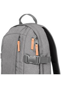 Sac à dos gris en tissu texturé, avec des zips en cuir et une boucle en plastique. Conçu avec une poignée sur le dessus et des bretelles rembourrées.