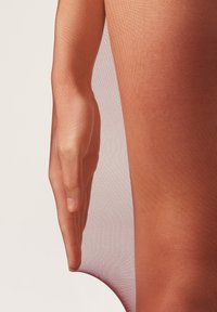 Tights translúcidos y texturizados en un degradado de melocotón a rojo intenso, combinados con una mano de tono de piel natural sosteniendo suavemente la tela.