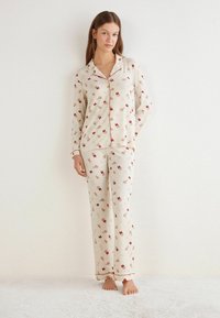 Kremowy zestaw piżamowy z czerwonym wzorem kwiatowym, z guzikiem z przodu, długimi rękawami oraz pasującymi luźnymi spodniami wykończonymi na czerwono.