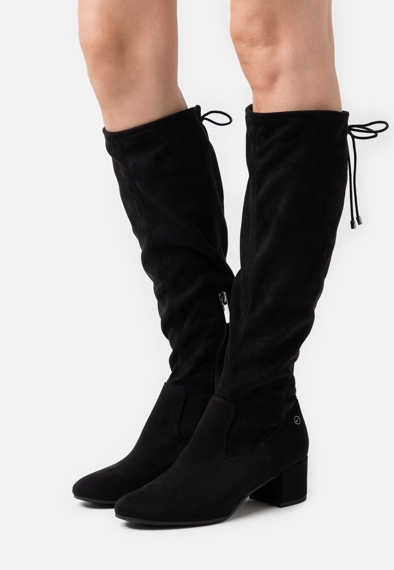 Bottes noires au-dessus du genou en suède doux, avec un talon bloc, une fermeture éclair sur le côté et un lien ajustable en haut pour un maintien sécurisé.