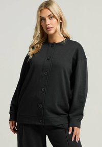 Cárdigan negro de gran tamaño con cuello redondo, mangas largas y cierre de seis botones. Fabricado con un tejido suave y de textura lisa.