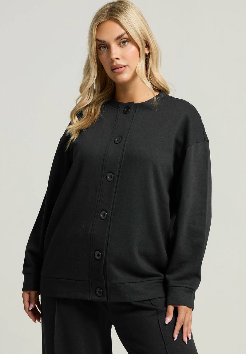 Cárdigan negro de gran tamaño con cuello redondo, mangas largas y cierre de seis botones. Fabricado con un tejido suave y de textura lisa.