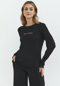Czarna bluzka z długim rękawem wykonana z miękkiego materiału. Na przodzie delikatny haft tekstu "Mon Amie". Prosty, okrągły dekolt.