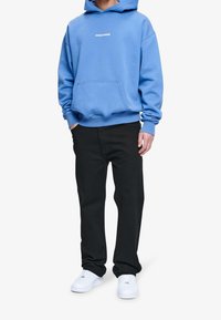 Blå sweatshirt med huva och framficka, med texten "PEGADOR." Bärs med svarta byxor och vita sneakers.