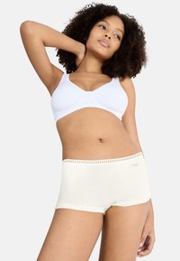 Hvid blød bh og cremefarvede shorts med blonderkant. Materialerne er glatte, tætsiddende og elastiske med delikate detaljer på linningen.