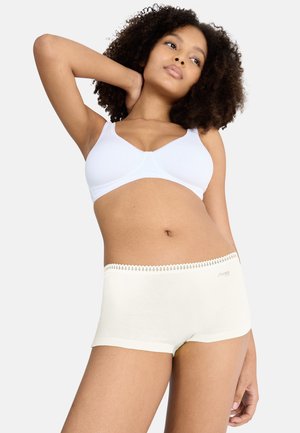 Weißer, weicher BH und cremefarbene Shorts mit Spitzenbesatz. Die Materialien sind glatt, eng anliegend und dehnbar, mit zarten Akzenten am Bund.