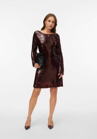 Vinrød paljettkjole med lange ermer, rund halslinning og en vid nederkant, kombinert med en svart clutch og spisse hæler.